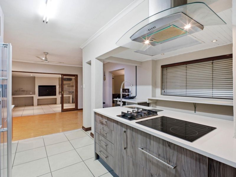 Modern kitchen featuring a dual gas and electric cooktop, glass extractor fan, stone countertops, and sleek cabinetry, flowing into an adjacent living area.