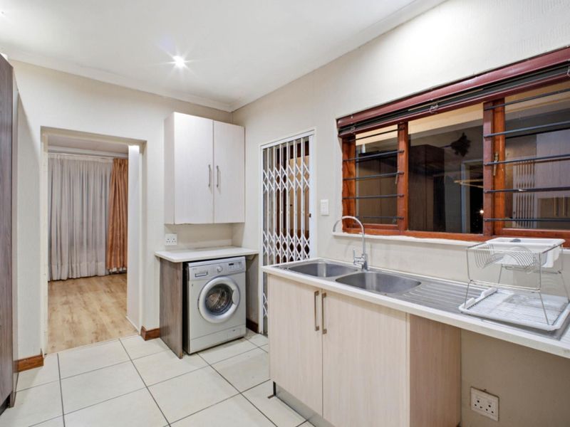 Functional laundry area featuring built-in cabinetry, a double stainless steel sink, tiled flooring, and a secure window with security bars.