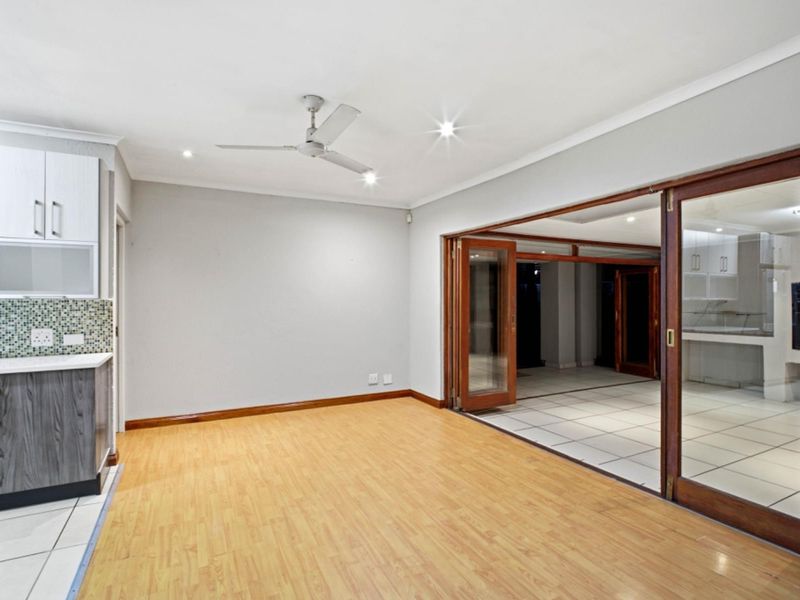 Spacious open-plan living area featuring laminate flooring, recessed lighting, a ceiling fan, and large wooden folding doors leading to an adjacent tiled space.