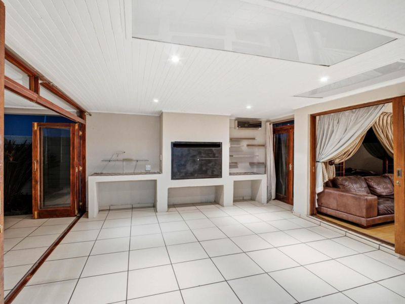Spacious covered patio featuring a built-in braai, tiled flooring, and large timber sliding doors providing seamless access to the interior living areas.