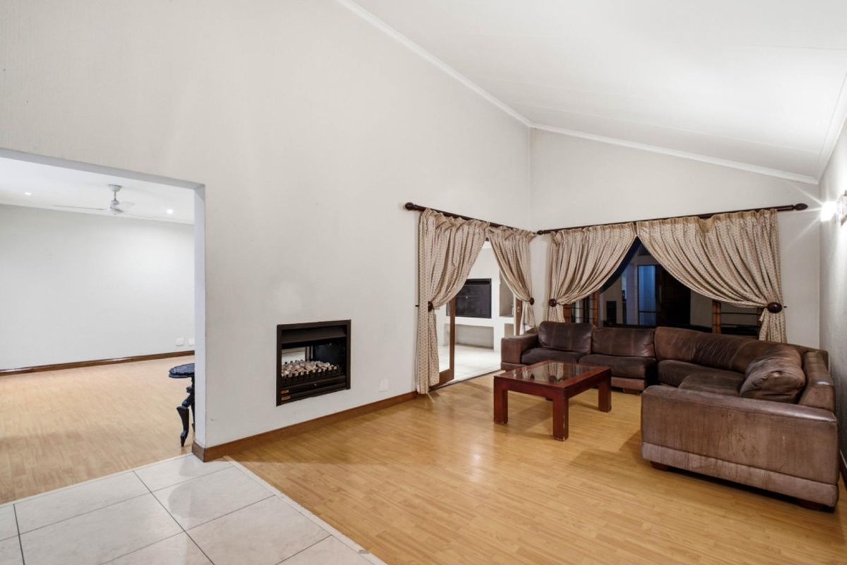Spacious living room featuring a vaulted ceiling, built-in fireplace, and a combination of laminate and tiled flooring with access to an adjacent room.