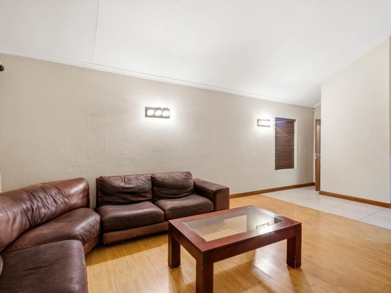 A spacious living room featuring a combination of laminate and tiled flooring, wall-mounted lighting, and neutral textured walls.