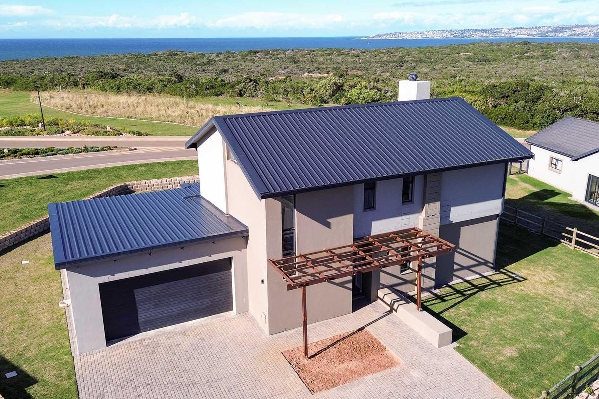 Aerial view of a modern double-story house featuring a metal roof, paved driveway, attached garage, and a timber pergola in a coastal estate setting.