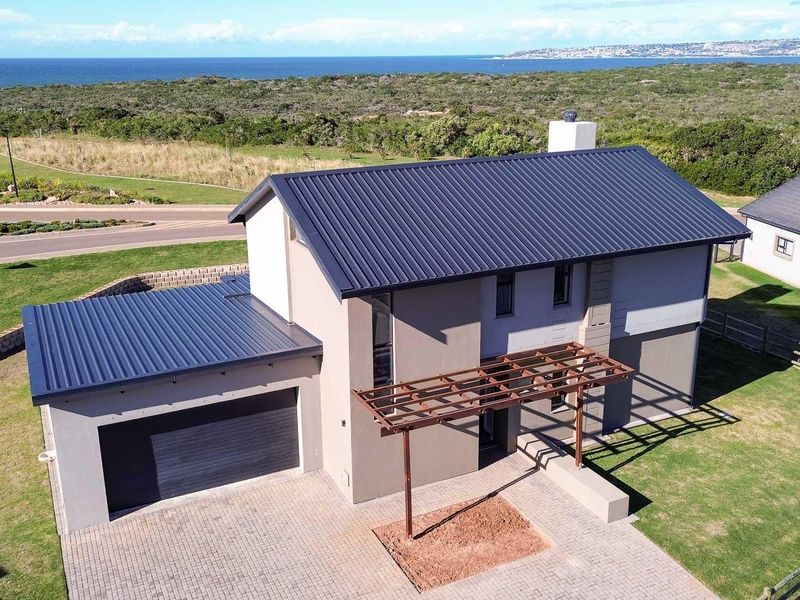 Aerial view of a modern double-story house featuring a metal roof, paved driveway, attached garage, and a timber pergola in a coastal estate setting.
