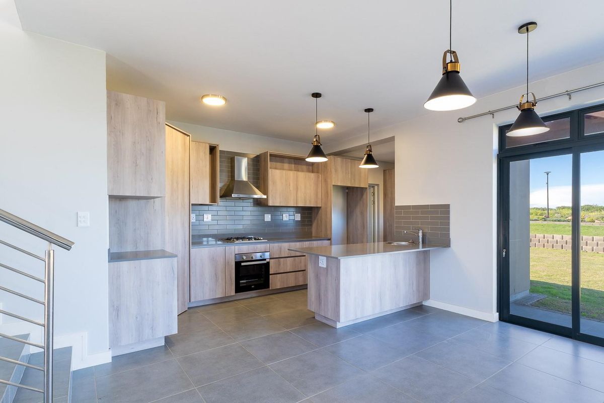 Modern open-plan kitchen featuring light wood-grain cabinetry, stone countertops, integrated stainless steel appliances, and direct access to the rear garden through sliding doors.