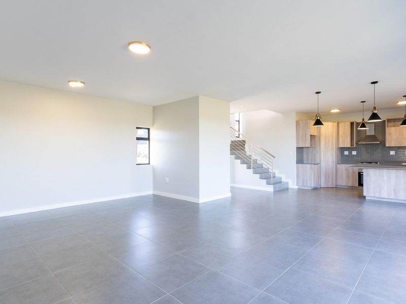 Spacious open-plan living area featuring modern tiled floors, a contemporary kitchen with built-in cabinetry, and a staircase leading to the upper level.