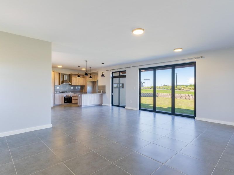 Spacious open-plan living and kitchen area featuring modern cabinetry, tiled floors, and large sliding glass doors leading to the garden.