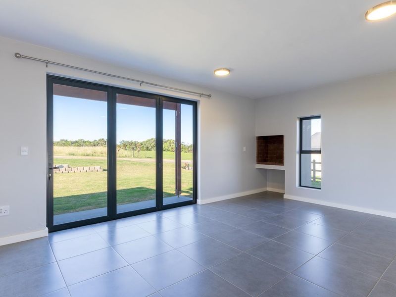 Spacious, modern living area featuring large aluminium sliding doors, neutral tiled flooring, and a built-in fireplace, offering seamless access to the outdoor space.