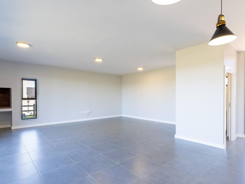 Spacious, modern open-plan living area featuring large format floor tiles, recessed lighting, a built-in fireplace, and direct access to an outdoor patio.