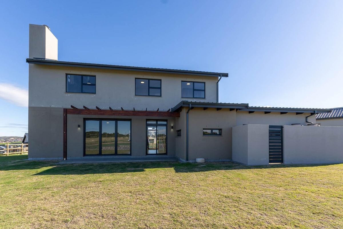 Rear view of a modern two-story house featuring a plastered facade, timber pergola, large sliding glass doors, and a spacious backyard.