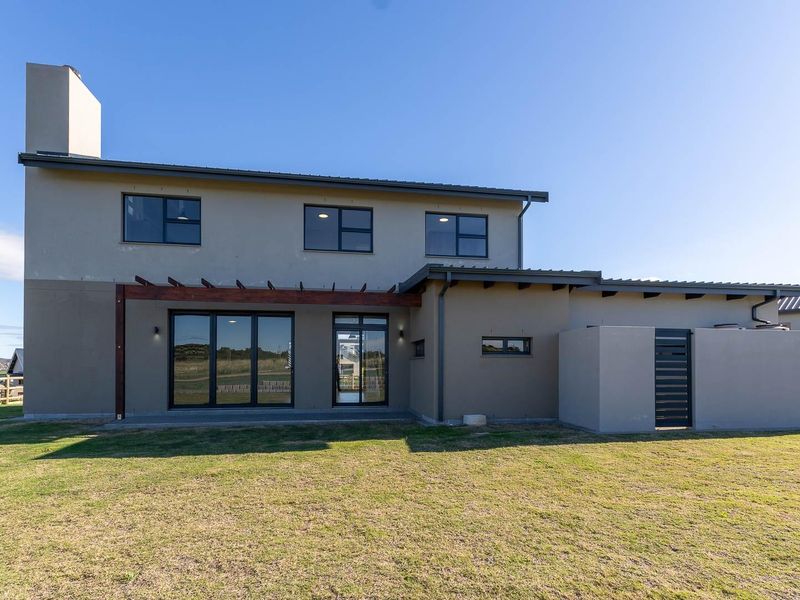 Rear view of a modern two-story house featuring a plastered facade, timber pergola, large sliding glass doors, and a spacious backyard.