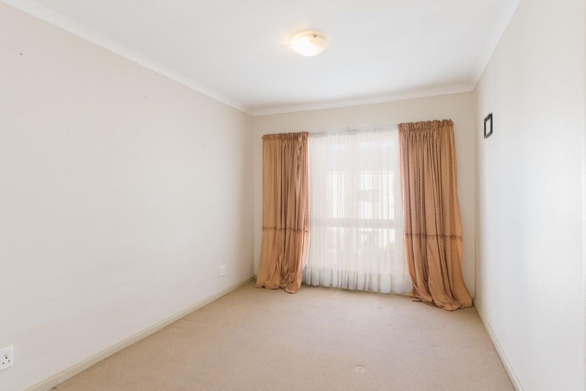 A clean, empty bedroom featuring neutral wall finishes, carpeted flooring, and large windows with existing curtain rails.