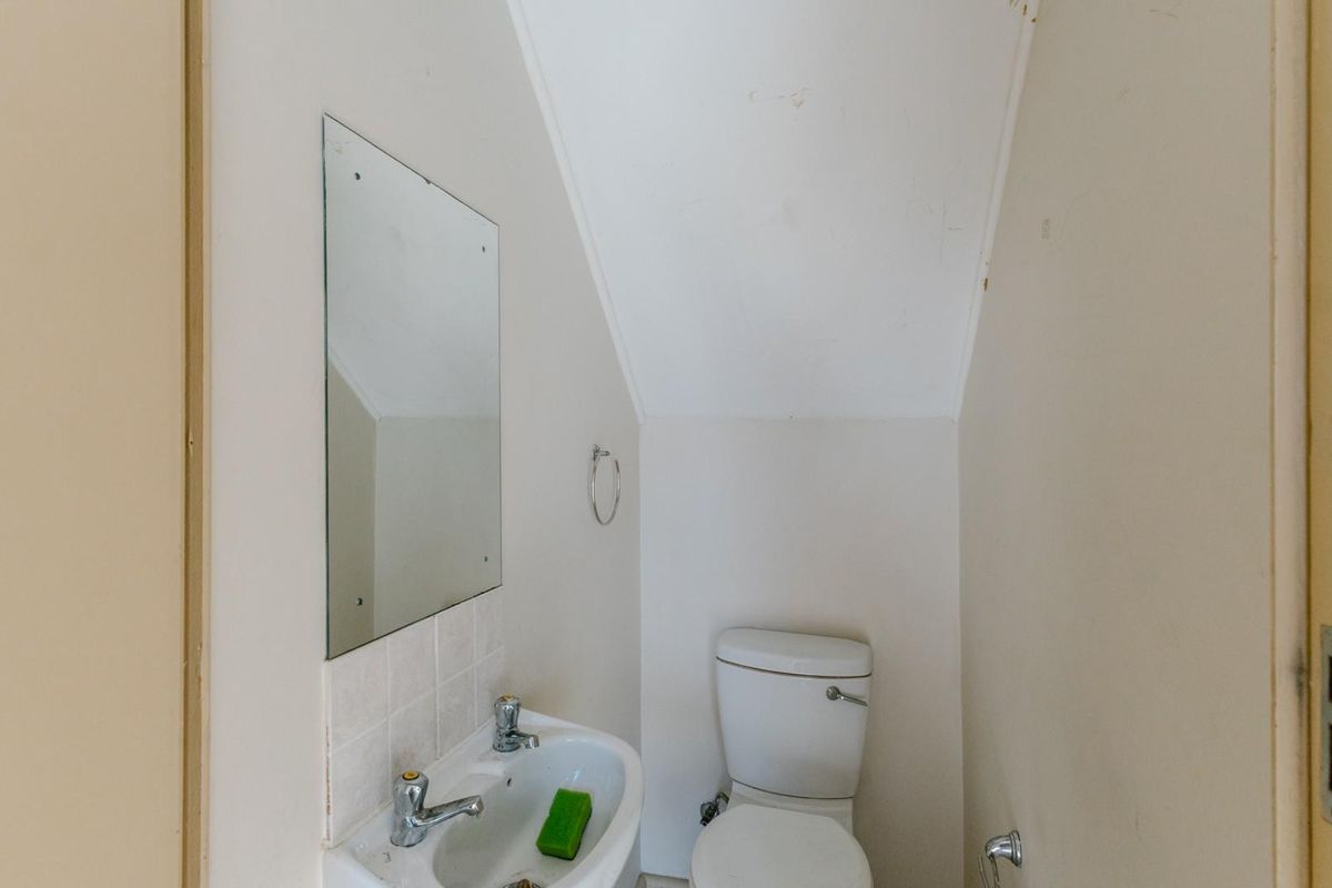 A compact guest bathroom featuring a white pedestal basin, toilet, and wall-mounted mirror, requiring minor cosmetic updates to refresh the space.