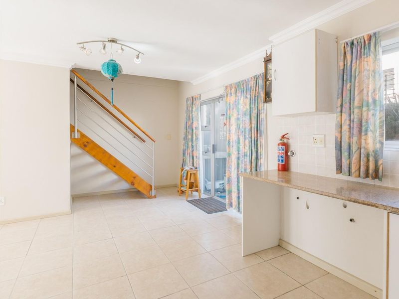Open plan living area featuring tiled floors, a staircase with wooden treads, and a functional kitchenette with built-in cabinetry and sink.