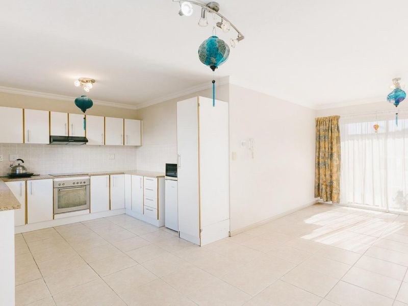 Open-plan kitchen and living area featuring tiled flooring, white cabinetry, built-in oven, and sliding glass doors leading to the exterior.