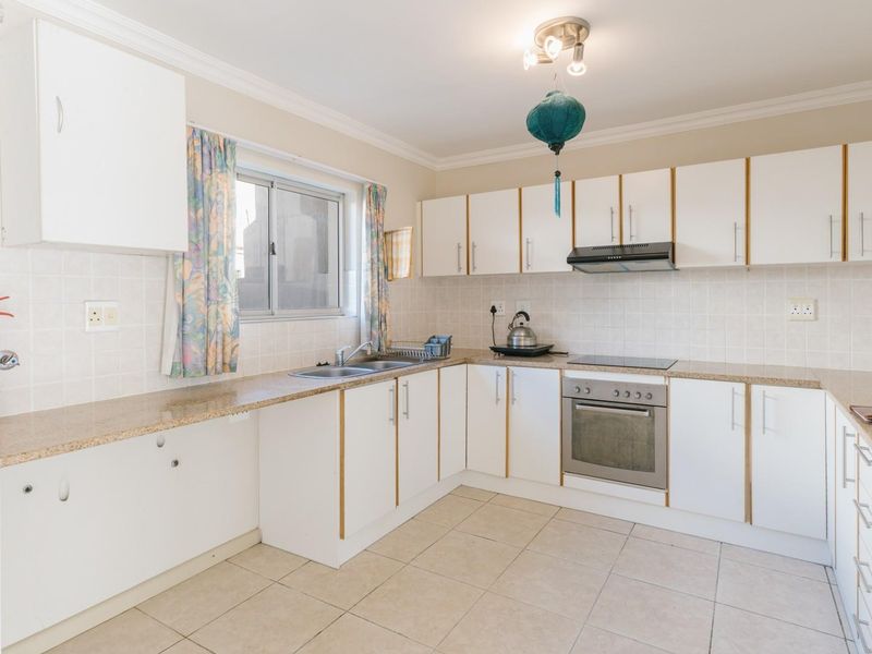 A functional kitchen featuring white cabinetry, granite countertops, tiled backsplash, and integrated appliances including an oven, hob, and extractor fan.