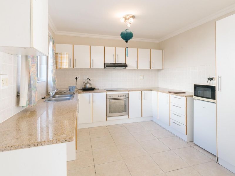 Functional kitchen featuring white cabinetry, laminate countertops, tiled backsplash, and integrated electric oven and hob with extractor fan.