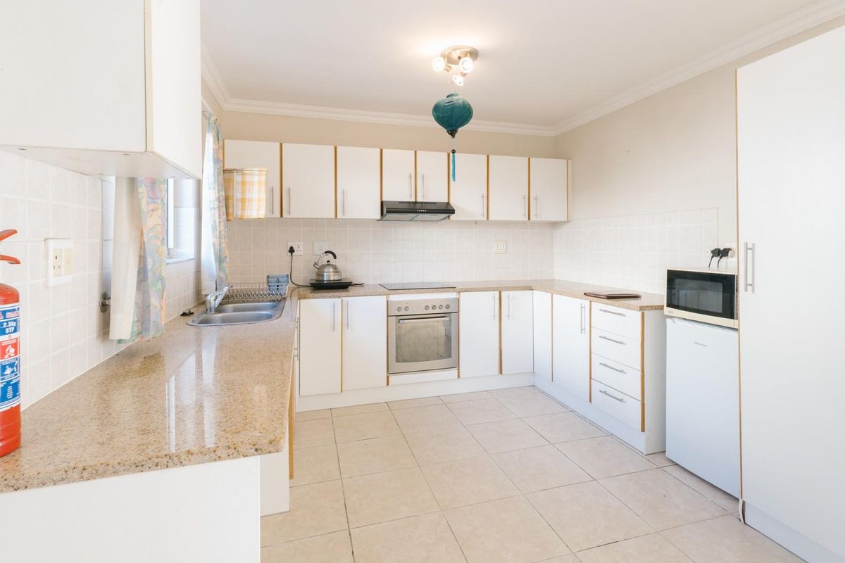 Functional kitchen featuring white cabinetry, laminate countertops, tiled backsplash, and integrated electric oven and hob with extractor fan.