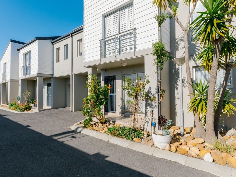 A row of modern townhouse units featuring weatherboard cladding, private balconies, and paved driveway access with landscaped garden beds.