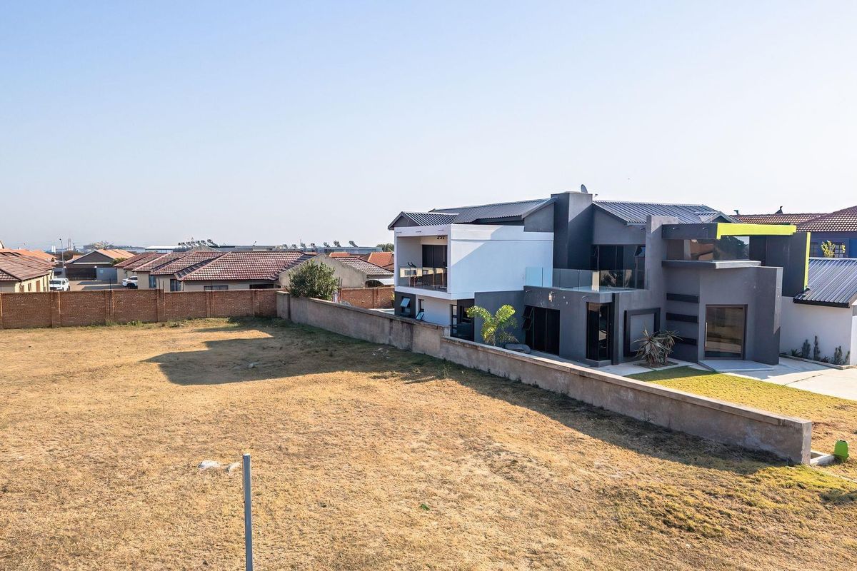 Aerial view of a residential property featuring a large vacant plot adjacent to a modern multi-story home with a boundary wall.