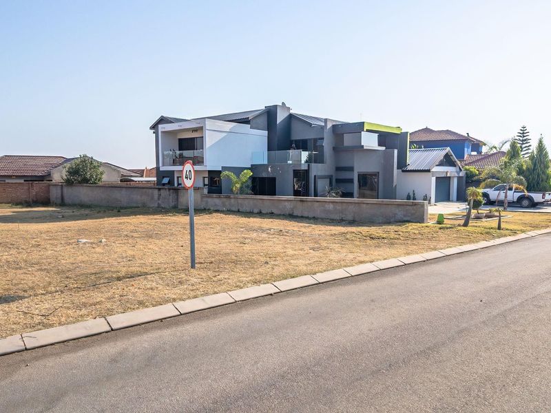 A vacant residential plot situated on a paved street, offering a clear view of the adjacent modern multi-story residential property.