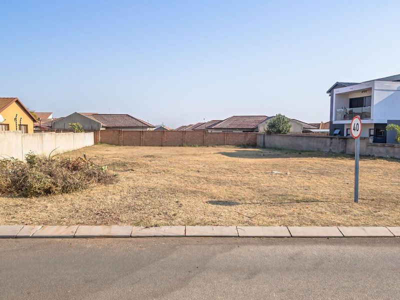A vacant residential plot of land featuring a perimeter wall, situated in a developed neighborhood with street access.