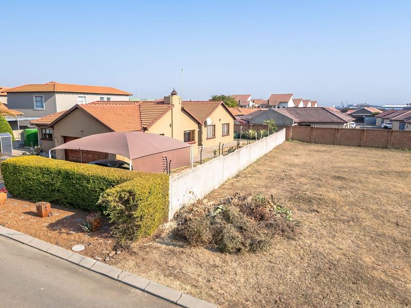 Aerial view of a vacant residential plot adjacent to an existing property with perimeter walling and electric fencing in a suburban neighborhood.