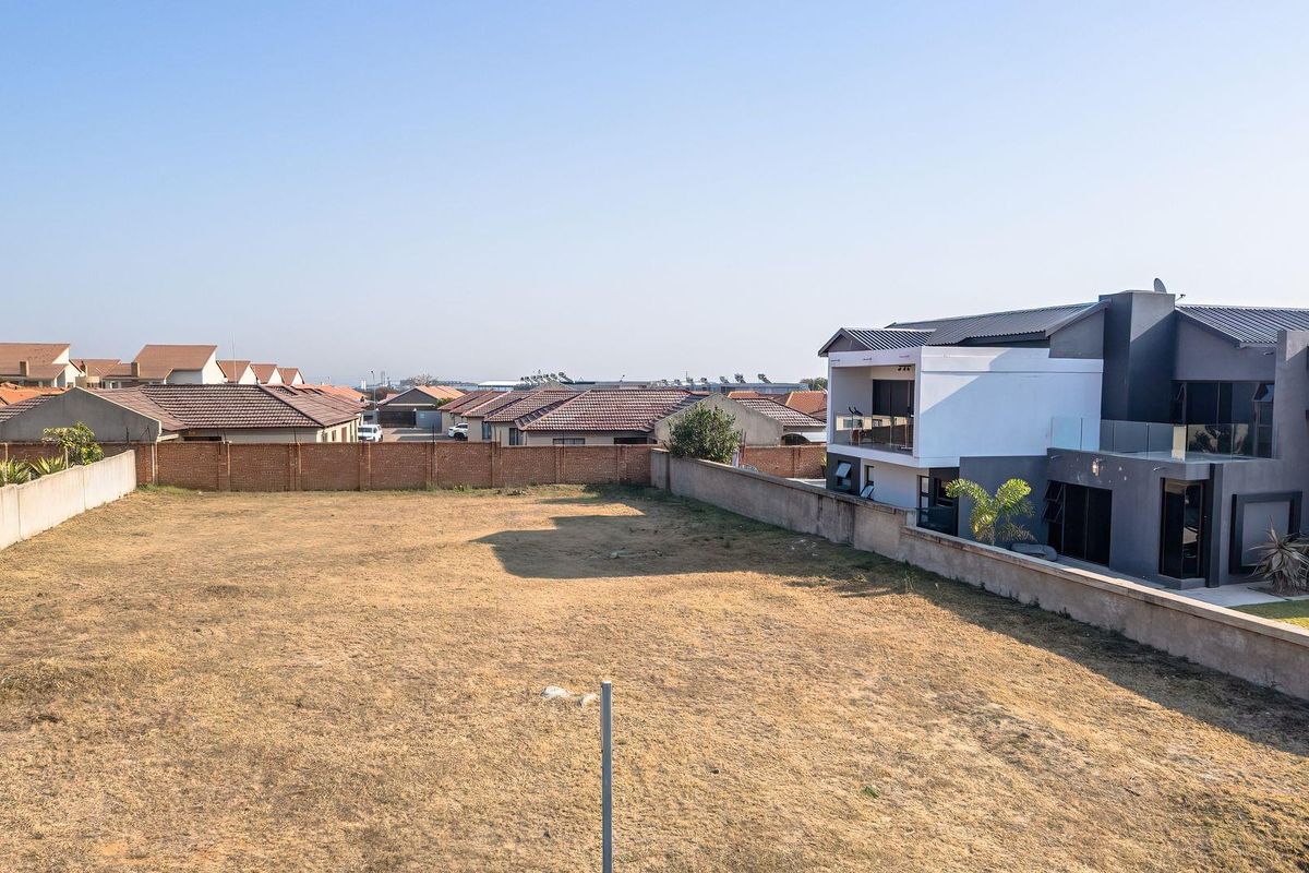 An aerial view of a vacant residential plot enclosed by perimeter brick and concrete boundary walls in a developed suburban neighborhood.