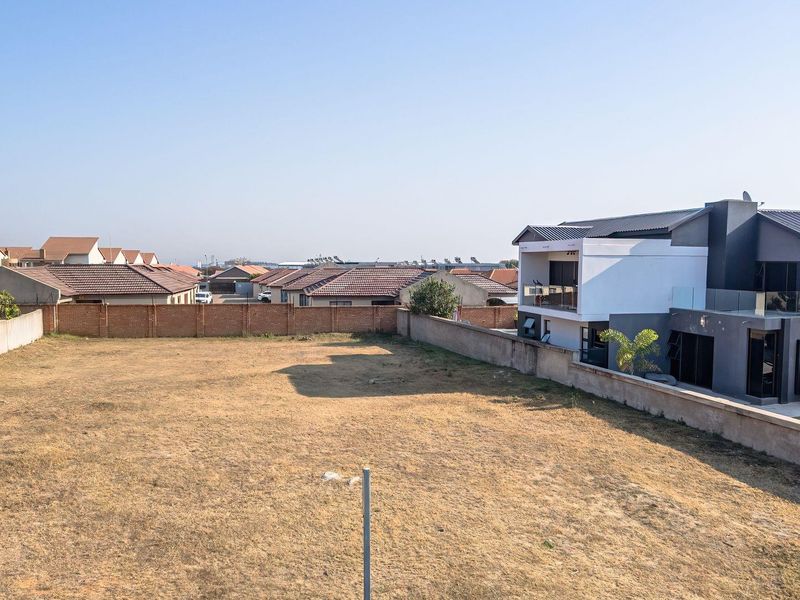 An aerial view of a vacant residential plot enclosed by perimeter brick and concrete boundary walls in a developed suburban neighborhood.