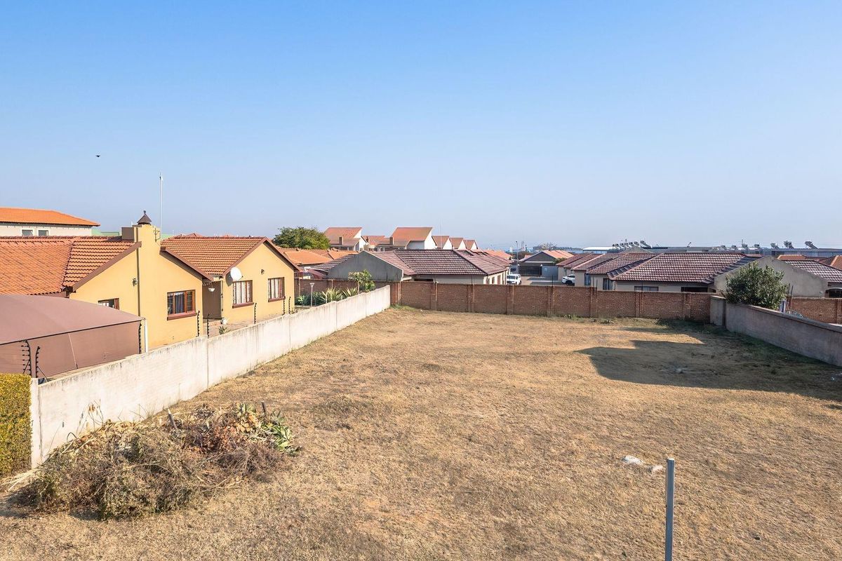 An elevated view of a vacant residential plot enclosed by perimeter brick and concrete boundary walls with electric fencing in a suburban neighborhood.