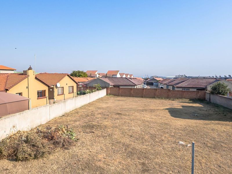 An elevated view of a vacant residential plot enclosed by perimeter brick and concrete boundary walls with electric fencing in a suburban neighborhood.