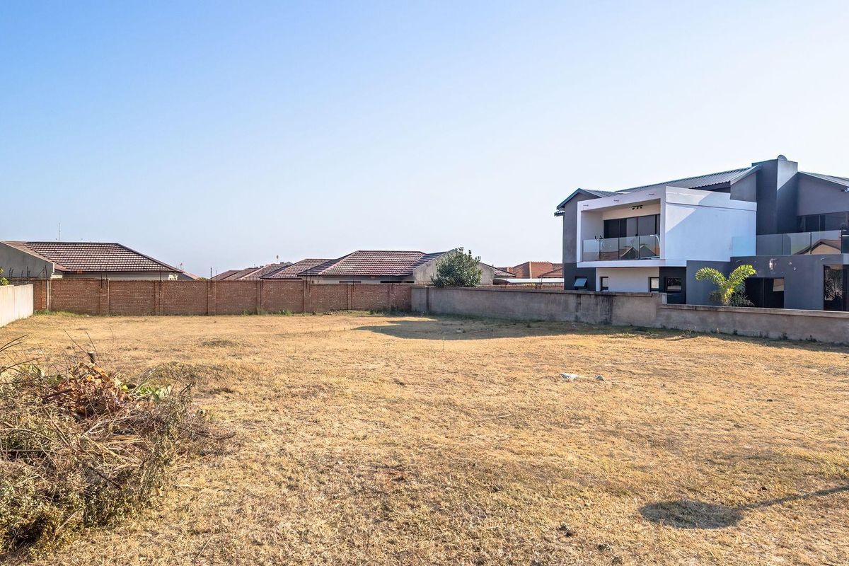 A vacant residential plot featuring dry grass and enclosed by perimeter brick boundary walls, situated in a developed neighborhood.
