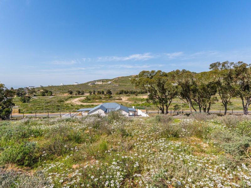 A scenic view overlooking a vacant residential plot with natural vegetation, surrounding landscape, and distant neighborhood houses.