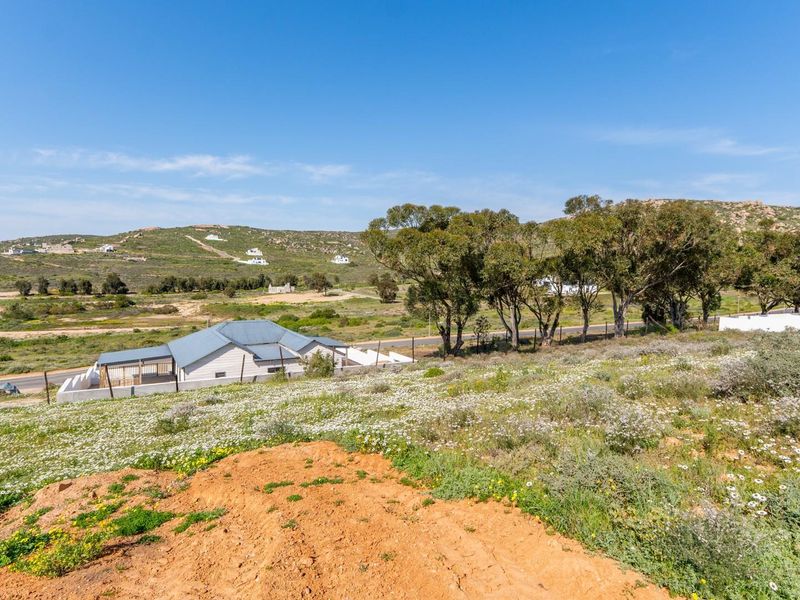 A scenic view overlooking a vacant residential plot with natural vegetation, mature trees, and surrounding landscape.