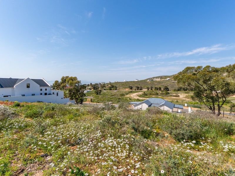 A scenic view overlooking a vacant residential plot with natural vegetation, surrounding hills, and nearby residential developments.