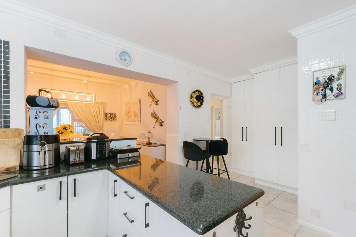 A well-maintained kitchen featuring granite countertops, white cabinetry, and a tiled backsplash, with an open-plan layout connecting to the adjacent living area.