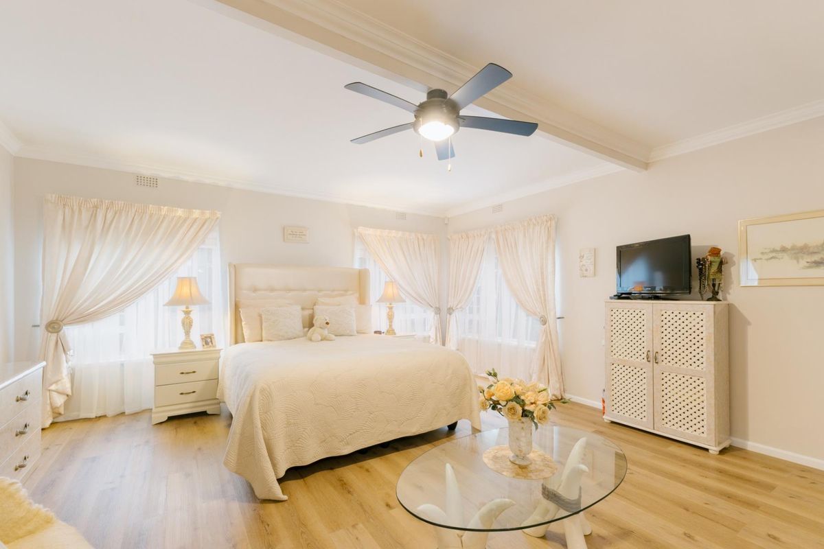 A well-maintained bedroom featuring light-toned laminate flooring, crown molding, and a central ceiling fan, creating a bright and comfortable living space.