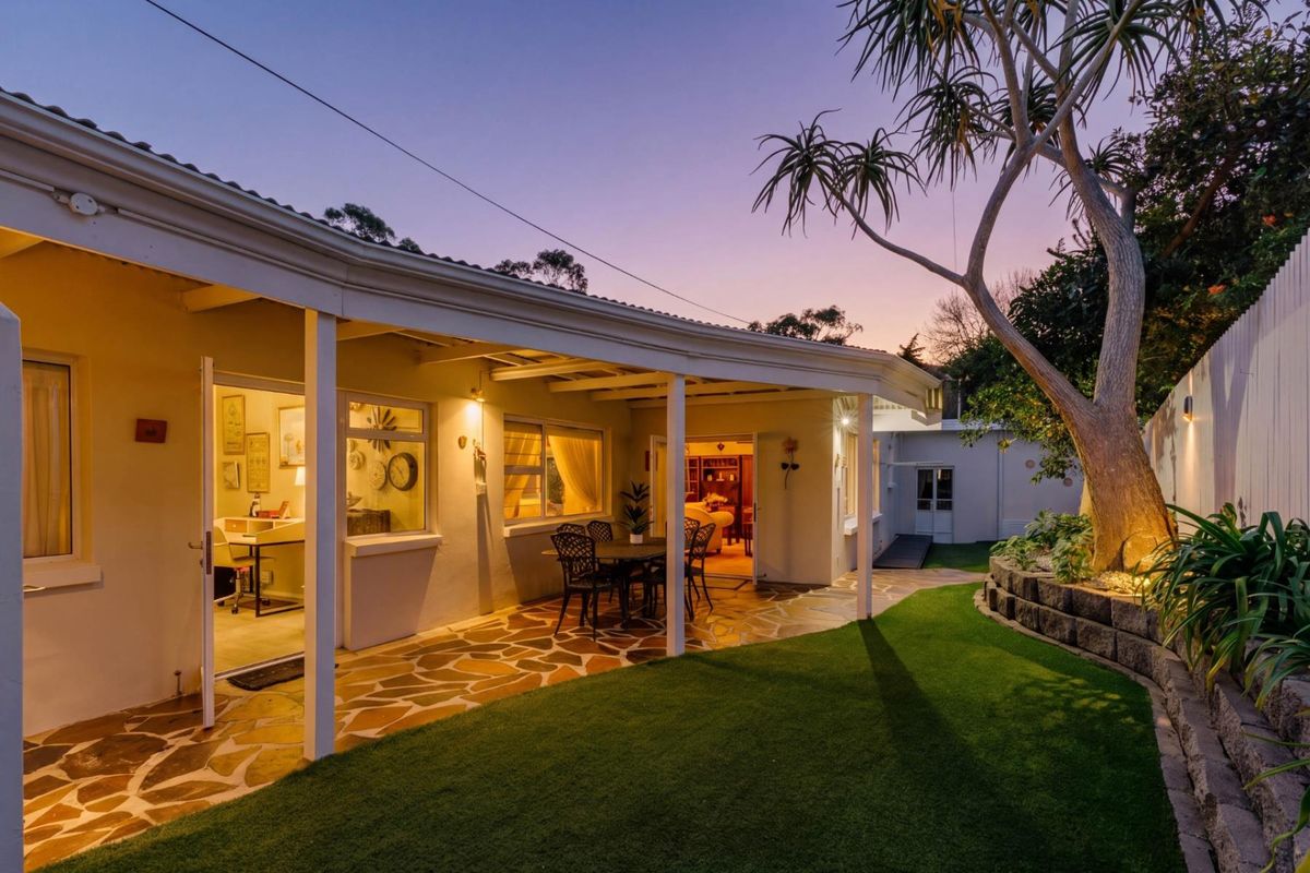A well-maintained rear exterior featuring a covered patio with stone paving, overlooking a landscaped garden with a retaining wall and mature tree.