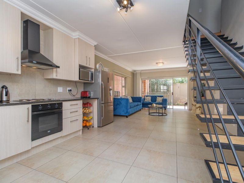 Open-plan living area featuring a modern kitchen with built-in appliances, tiled flooring, and a metal staircase leading to the upper level.