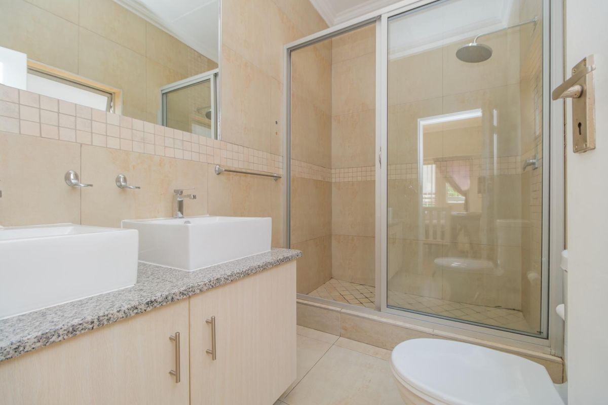 Modern bathroom featuring a double vanity with granite countertop, a glass-enclosed shower with a rain shower head, and neutral wall tiling.