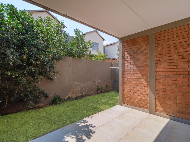A covered patio area featuring tiled flooring and a built-in braai, overlooking a small private garden with a boundary wall.