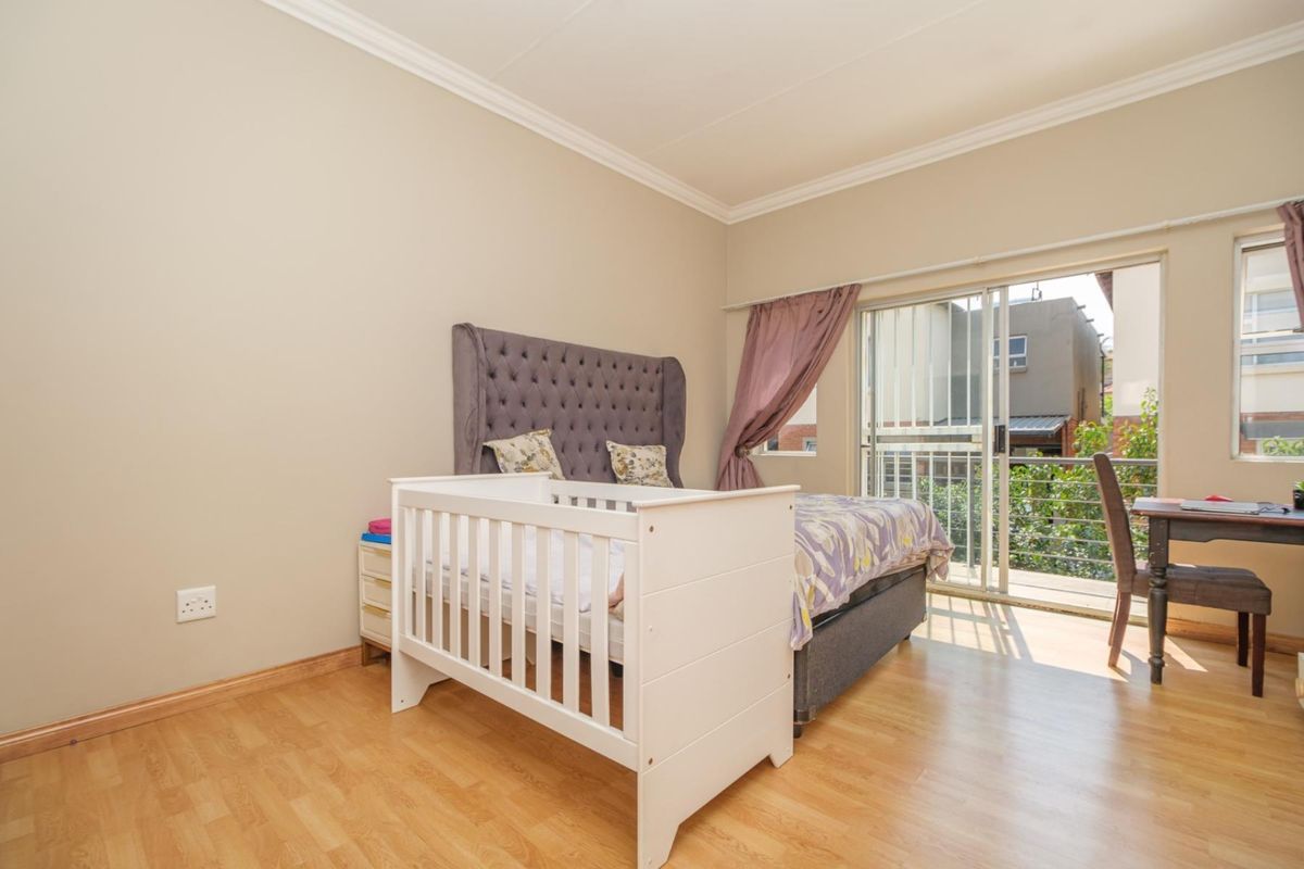 A well-lit bedroom featuring laminate flooring, coving, and a sliding glass door providing direct access to a private balcony.