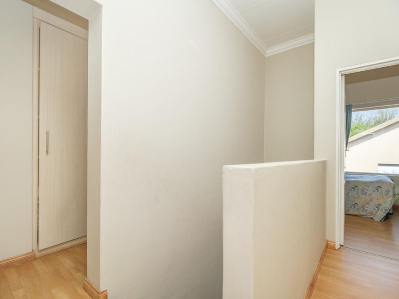 A clean, neutral hallway featuring laminate flooring, a built-in cupboard, and access to an adjacent bedroom.