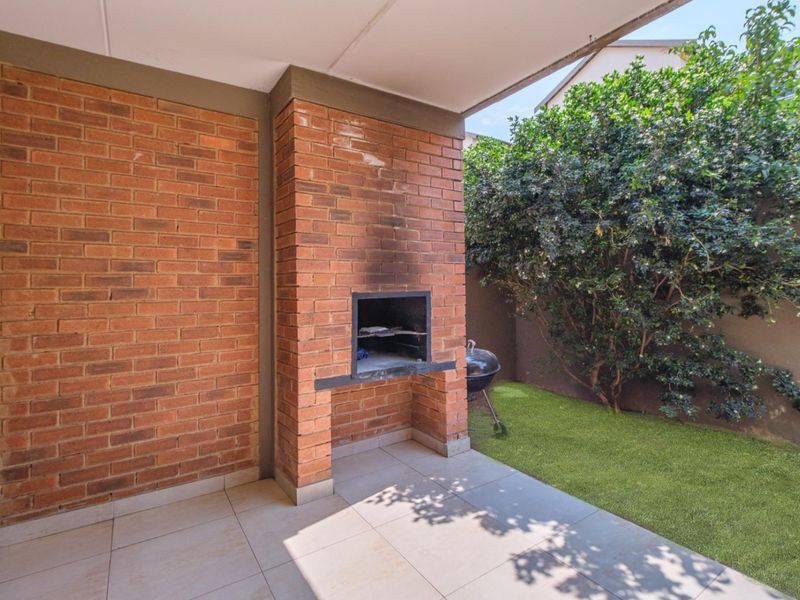 Covered patio area featuring a built-in brick braai and tiled flooring, overlooking a small private garden space.