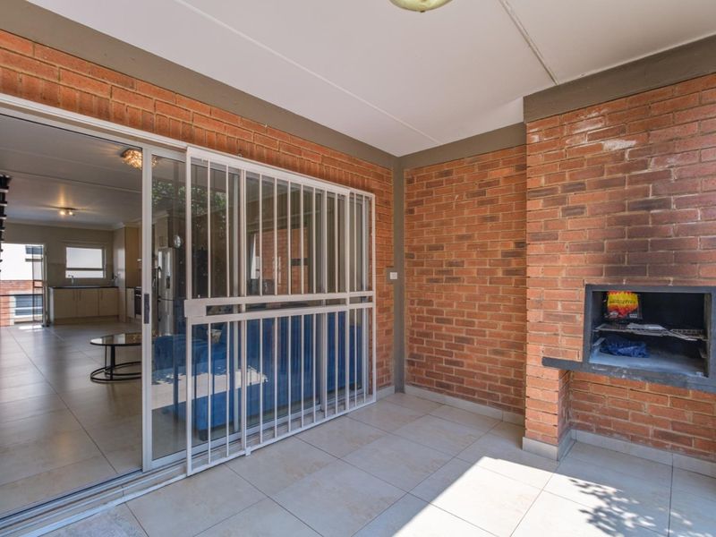 Covered patio featuring exposed brick walls, tiled flooring, and a built-in braai, providing a seamless transition to the interior living space.