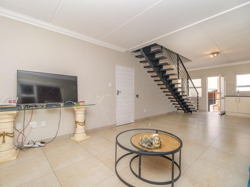Open-plan living area featuring tiled floors, a modern open-tread staircase, and a functional kitchen space with built-in cabinetry.