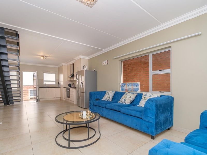 Open-plan living area featuring tiled floors, a modern staircase, and a functional kitchen with built-in cabinetry and appliances.
