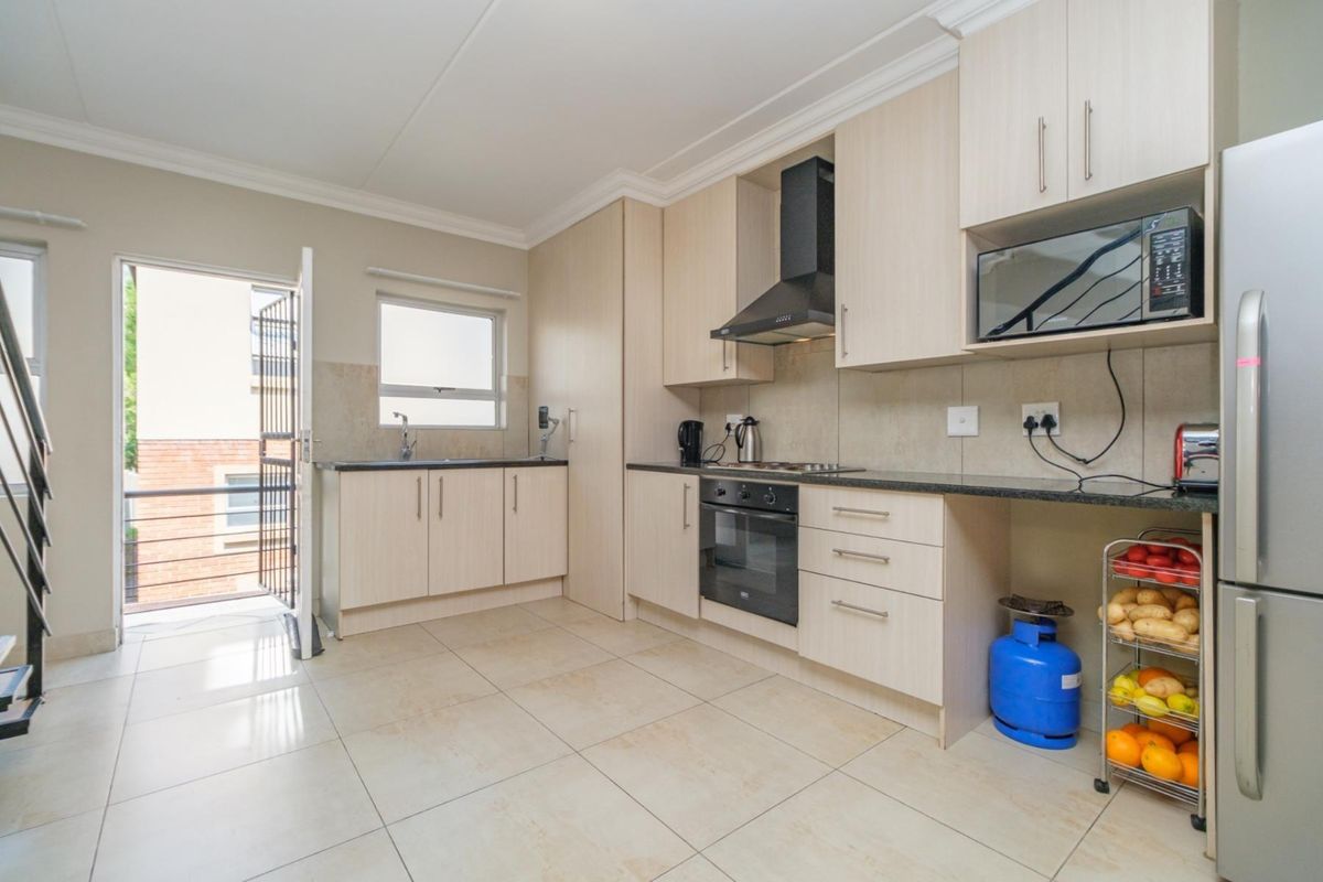 Modern kitchen featuring light wood cabinetry, granite countertops, built-in oven, hob, extractor fan, and tiled flooring with direct access to an outdoor balcony.