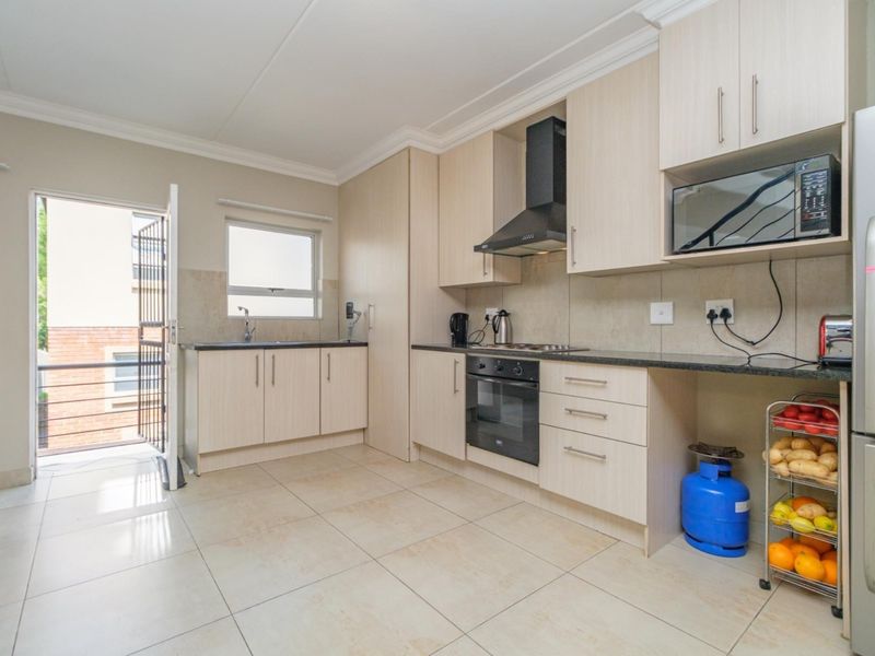 Modern kitchen featuring light wood cabinetry, granite countertops, built-in oven, hob, extractor fan, and tiled flooring with direct access to an outdoor balcony.