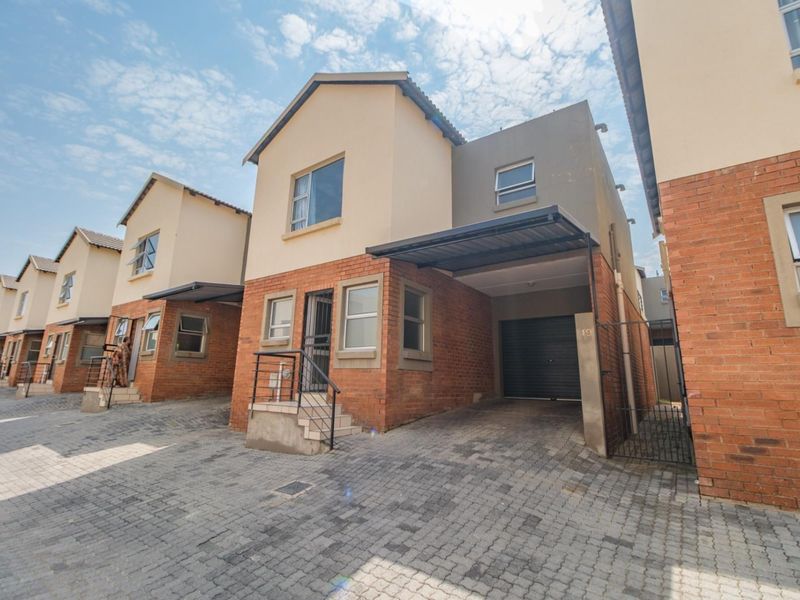 Front elevation of a townhouse complex featuring brick facades, paved driveways, integrated garages, and covered carports with secure gated access.
